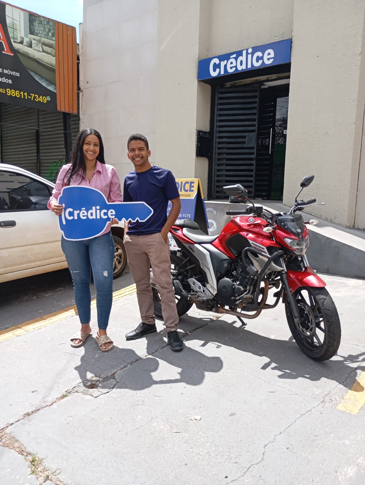 Clientes da Credice com a chave simbólica ao lado da moto conquistada