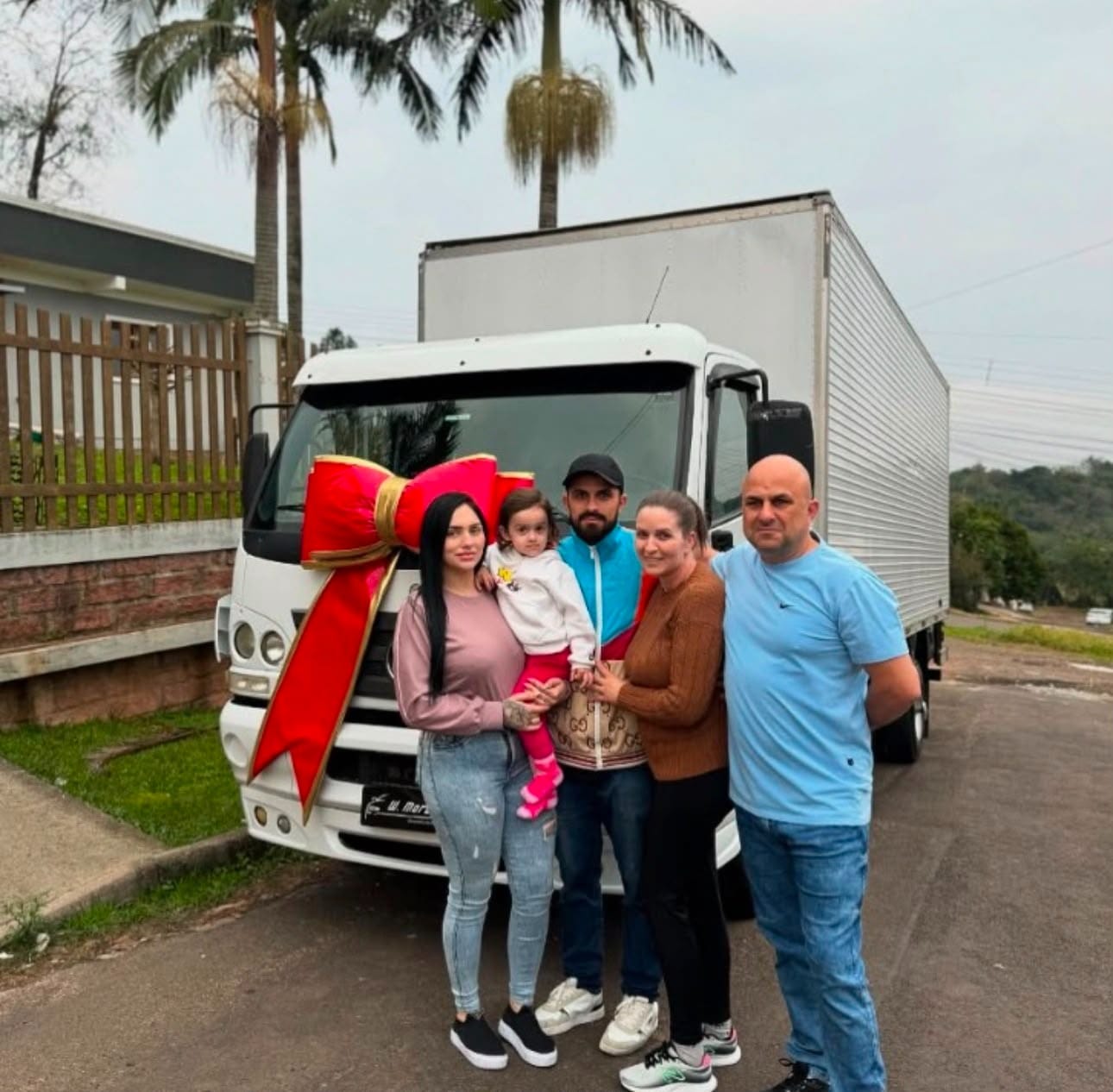 Família celebrando a entrega do caminhão baú com laço vermelho